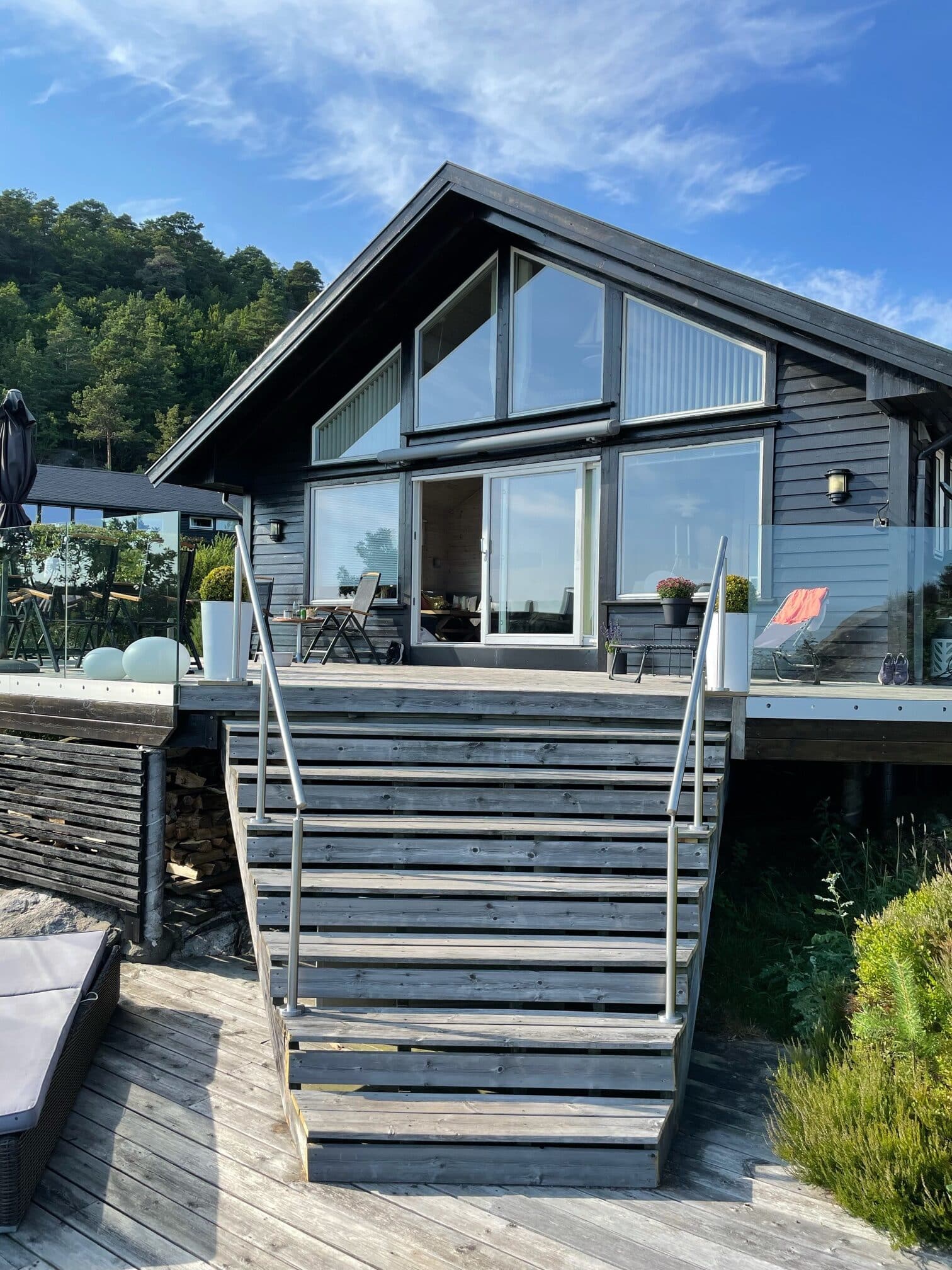 Outdoor wire handrails installed on both sides of a wide wooden staircase leading up to a black modern cabin with large windows and a deck.